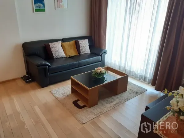 คอนโด ให้เช่าในKhlong Toei, Bangkok - ห้องนั่งเล่นสว่าง โซฟาหนังสีดำ โต๊ะกลาง และผ้าม่านโปร่งจากพื้นจรดเพดานรับแสงธรรมชาติ