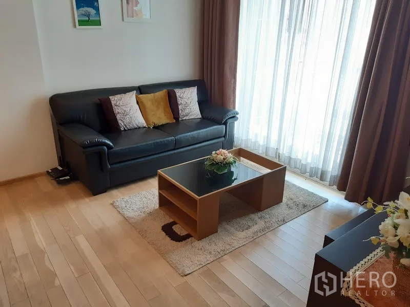 คอนโด ให้เช่าในKhlong Toei, Bangkok - ห้องนั่งเล่นสว่าง โซฟาหนังสีดำ โต๊ะกลาง และผ้าม่านโปร่งจากพื้นจรดเพดานรับแสงธรรมชาติ