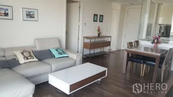 คอนโด ให้เช่าในBangkok - ห้องนั่งเล่นโซฟาหนังตัวแอล โต๊ะกลางสีขาว พื้นไม้ ใกล้โต๊ะอาหาร