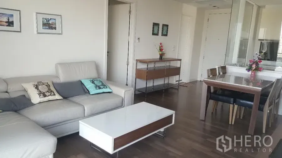 คอนโด ให้เช่าในBangkok - ห้องนั่งเล่นโซฟาหนังตัวแอล โต๊ะกลางสีขาว พื้นไม้ ใกล้โต๊ะอาหาร