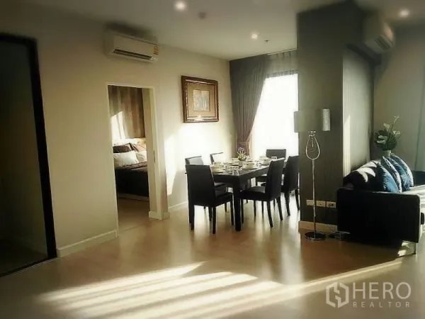 Condominium for rent or sale in Huai Khwang, Bangkok - Dining area set for six beside a sunlit window and doorway to a bedroom.