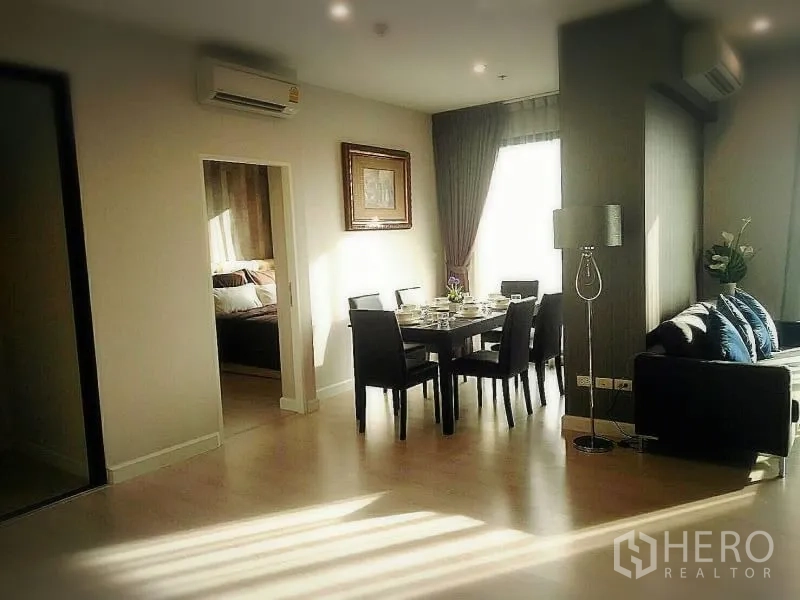 Condominium for rent or sale in Huai Khwang, Bangkok - Dining area set for six beside a sunlit window and doorway to a bedroom.