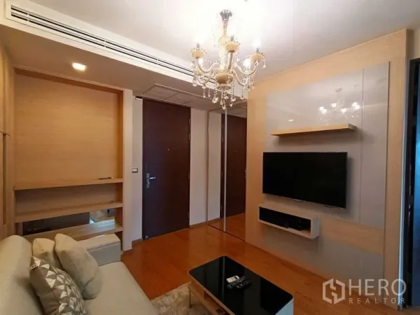 คอนโด ให้เช่าในRatchathewi, Bangkok - ห้องนั่งเล่นคอนโดในราชเทวี พื้นไม้ โคมระย้า ผนังบิลท์อินทีวี และโซฟาใกล้ทางเข้า