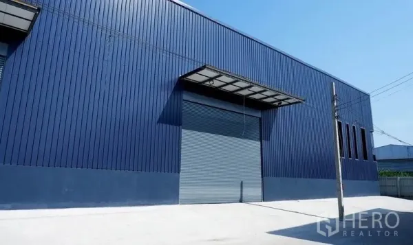 货栈 出租在Bueng Kum, Bangkok - 蓝色金属外墙仓库，配大卷闸门、带顶装卸区与宽阔混凝土车道，位于曼谷Bueng Kum。