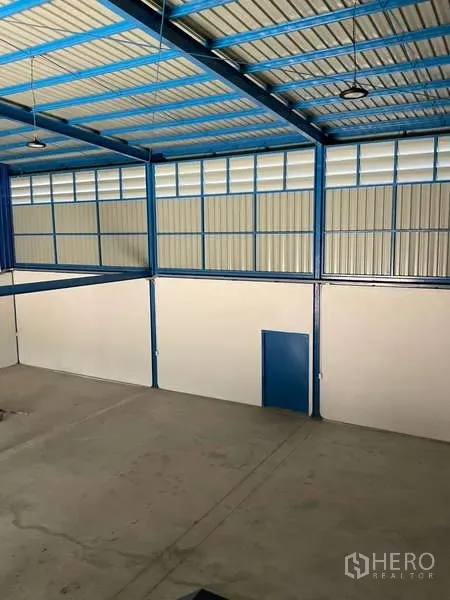 Warehouse for rent in Bang Bua Thong, Nonthaburi - High-ceiling warehouse interior with blue steel structure, ventilated panels and concrete floor.
