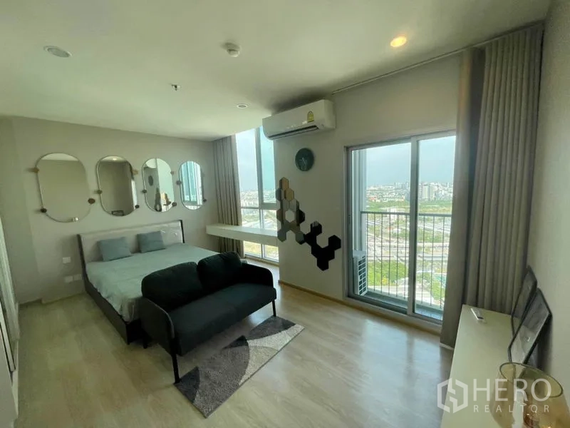 Condominium for rent in Huai Khwang, Bangkok - Airy bedroom with bed, sofa and sliding door to balcony overlooking Bangkok.