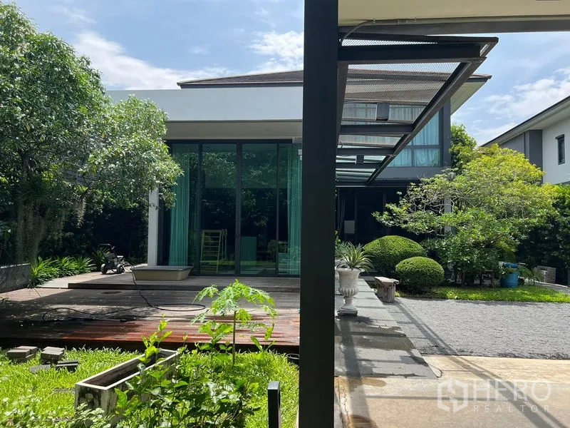 Detached House for sale in Bang Kapi, Bangkok - Side elevation showing a glass-walled room opening to a wooden deck and lawn.