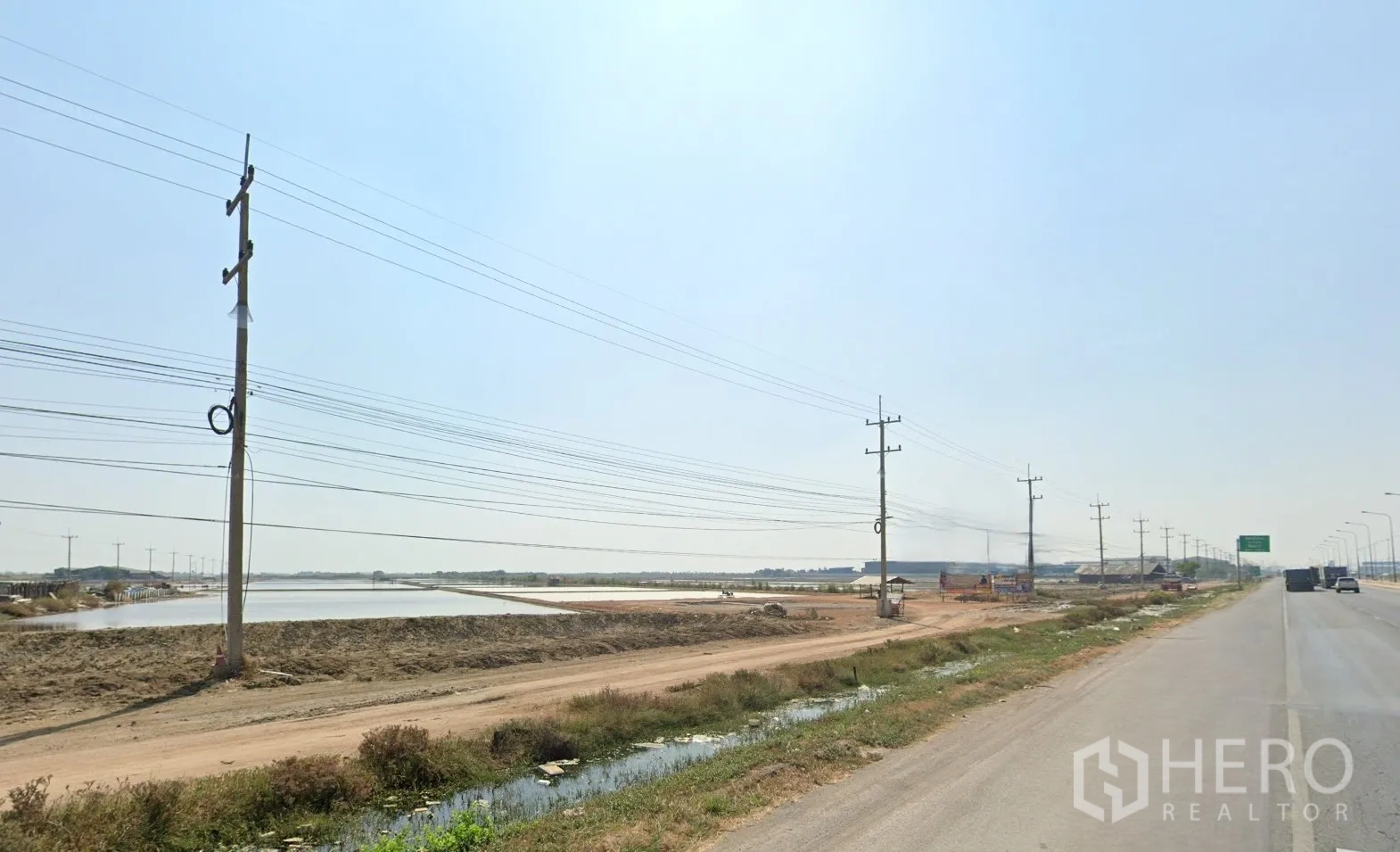 Land for sale in Mueang Samut Sakhon, Samut Sakhon - Roadside scene with dirt access track, power lines, and flat plots with ponds.