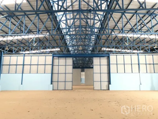 Warehouse for rent in Samut Prakan - Spacious warehouse interior showing blue steel trusses and central partition doors.