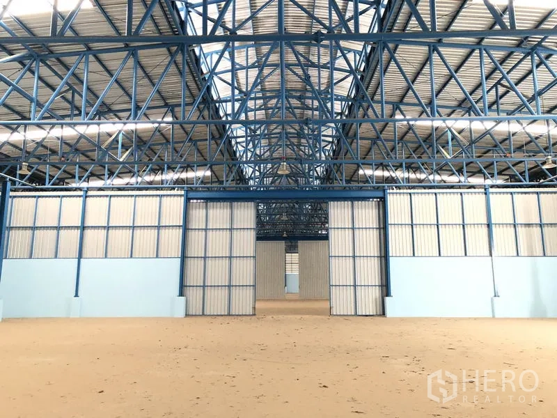 Warehouse for rent in Samut Prakan - Spacious warehouse interior showing blue steel trusses and central partition doors.