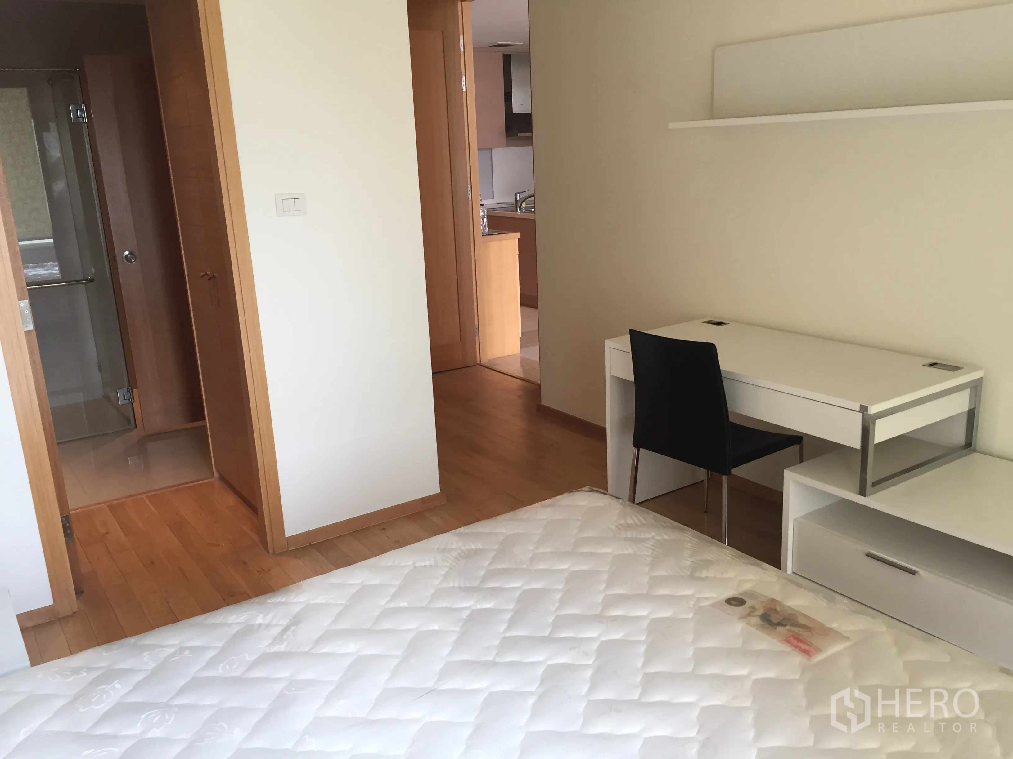 Condominium for rent in Sathon, Bangkok - Bedroom corner with white study desk, wall shelf, and doorway leading to the bathroom and kitchen area in a Bangkok condominium.