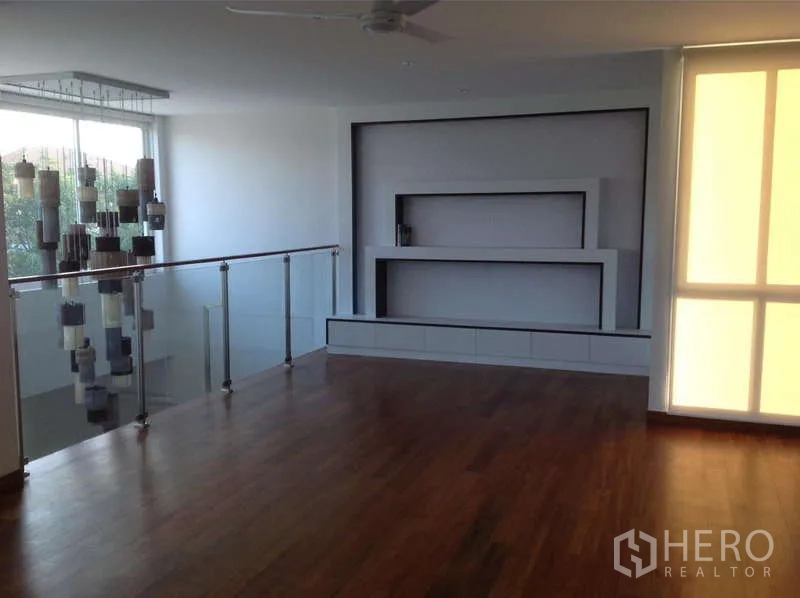 独立式住宅 出租在Lat Phrao, Bangkok - 二层多功能厅，木地板、玻璃栏杆与内置层架。