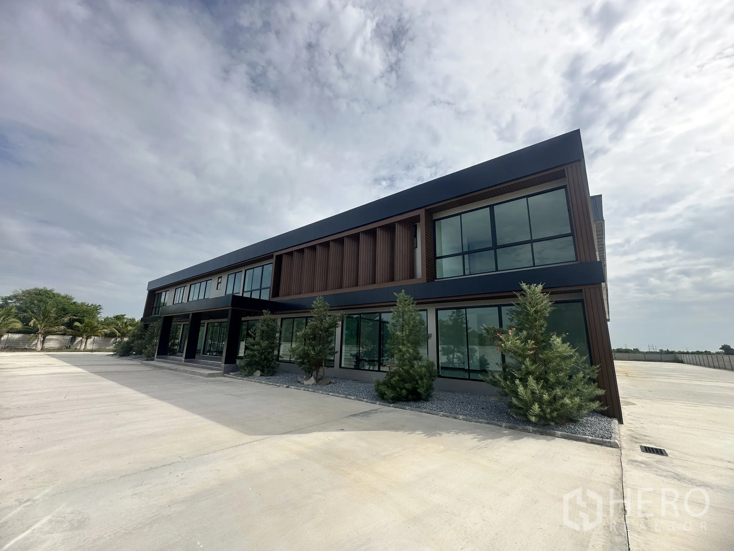 Factory for rent or sale in Bang Len, Nakhon Pathom - Contemporary two-storey office building with full-height glass and landscaped shrubs beside a wide concrete yard.