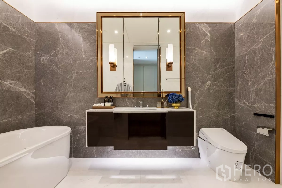 Condominium for rent or sale in Pathum Wan, Bangkok - Symmetrical bathroom view with tub, floating vanity and gold-framed mirror.