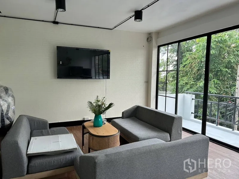 带办公室的家 出租或出售在Phra Khanong, Bangkok - 客厅区域，壁挂电视、灰色沙发及通往阳台的推拉门。