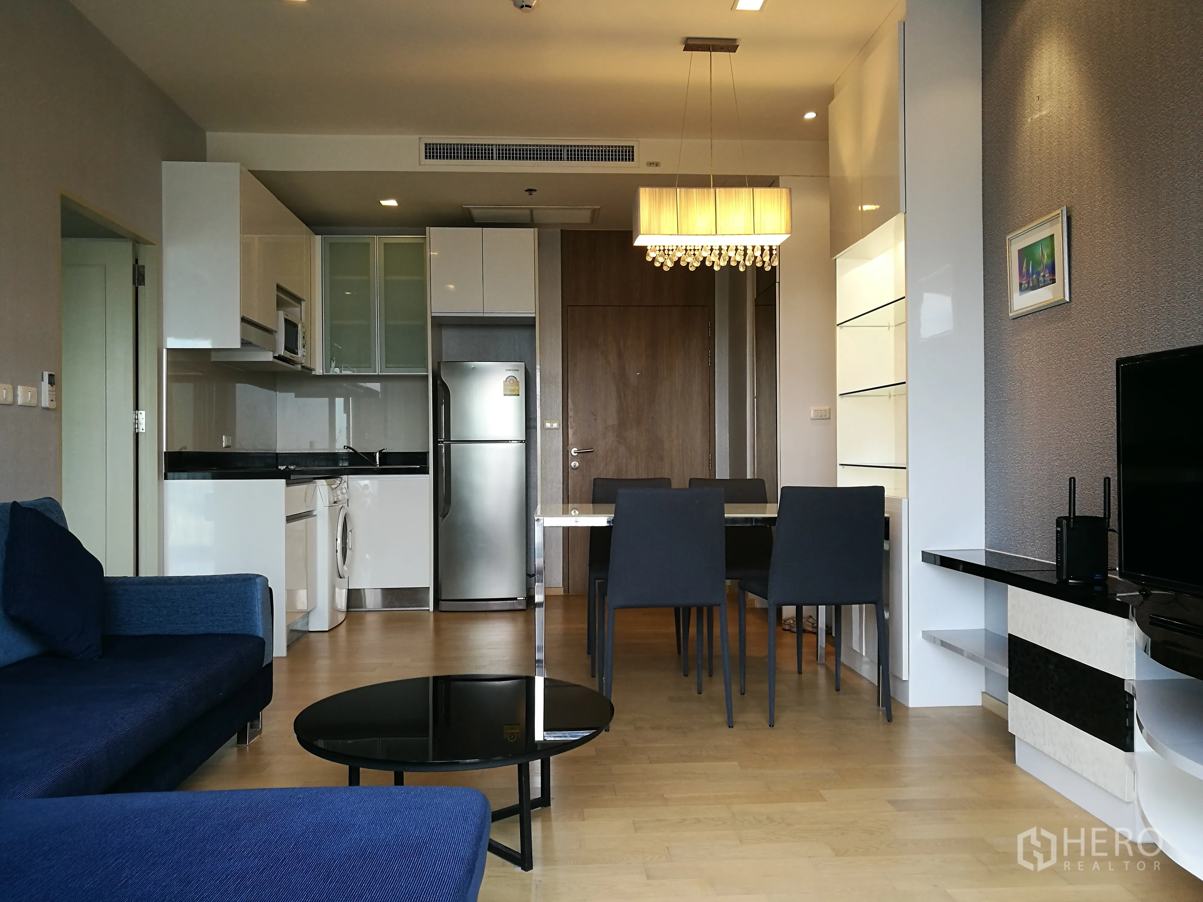 Condominium for rent in Watthana, Bangkok - Modern open kitchen with refrigerator, microwave, washing machine, and a dining table beneath a pendant light.
