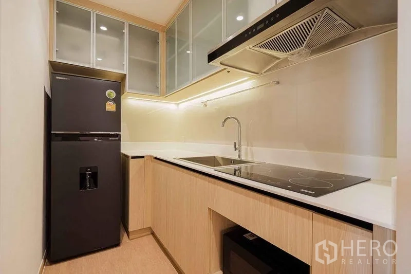 Condominium for rent in Watthana, Bangkok - Modern enclosed kitchen with black refrigerator, induction cooktop, and glass cabinets.