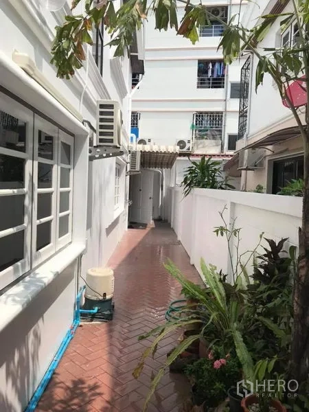 Detached House for rent in Khlong Toei, Bangkok - Tiled side walkway beside a white detached house with windows, AC units and potted plants