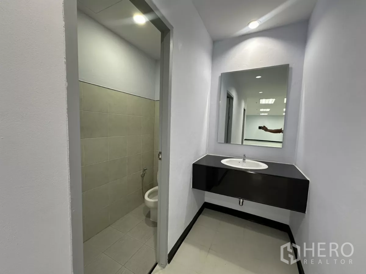 Office Space for rent - Close-up of vanity with mirror and sink beside a tiled private toilet.