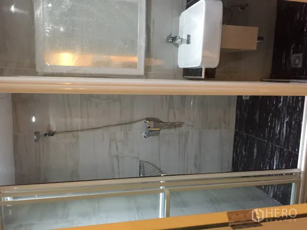Condominium for rent in Pathum Wan, Bangkok - Marble-tiled bathroom with glass-enclosed shower and wall-mounted sink.