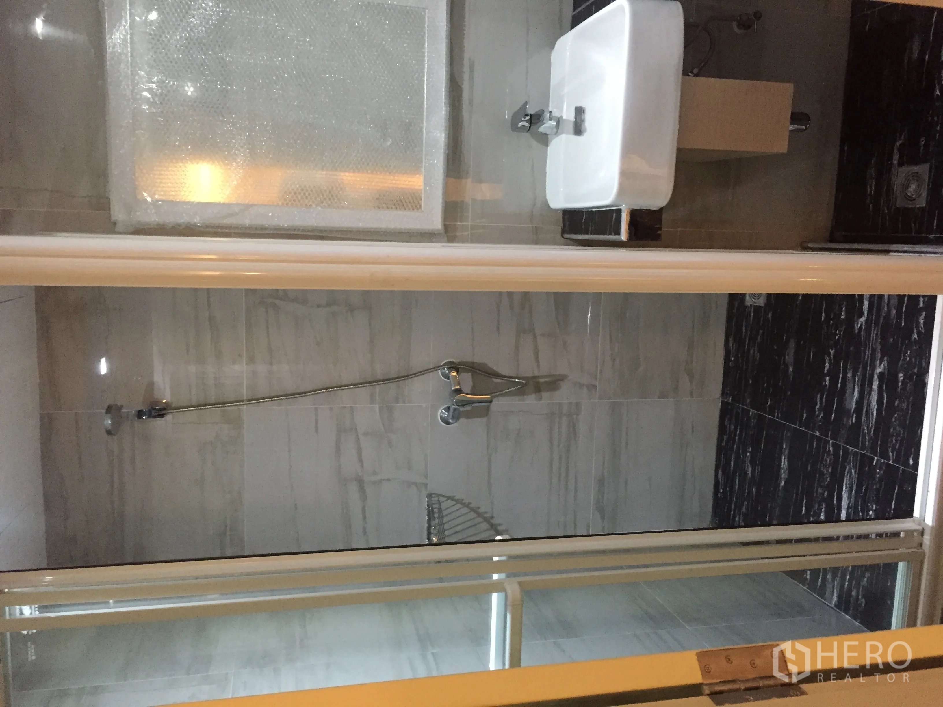 Condominium for rent in Pathum Wan, Bangkok - Marble-tiled bathroom with glass-enclosed shower and wall-mounted sink.