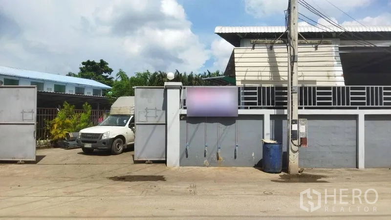 คลังสินค้า ขายในSamut Sakhon - ด้านหน้าทรัพย์ มีกำแพงและประตูเหล็กคู่ติดถนน พร้อมเสาไฟฟ้าริมทาง