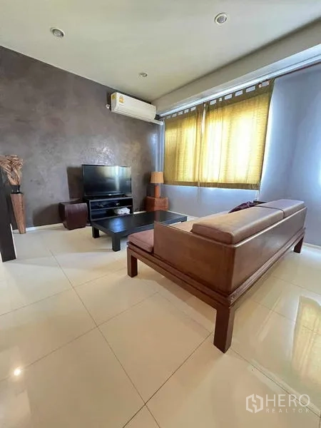 Condominium for rent in Ratchathewi, Bangkok - Living room with TV console, leather sofa, air conditioner, and large windows.