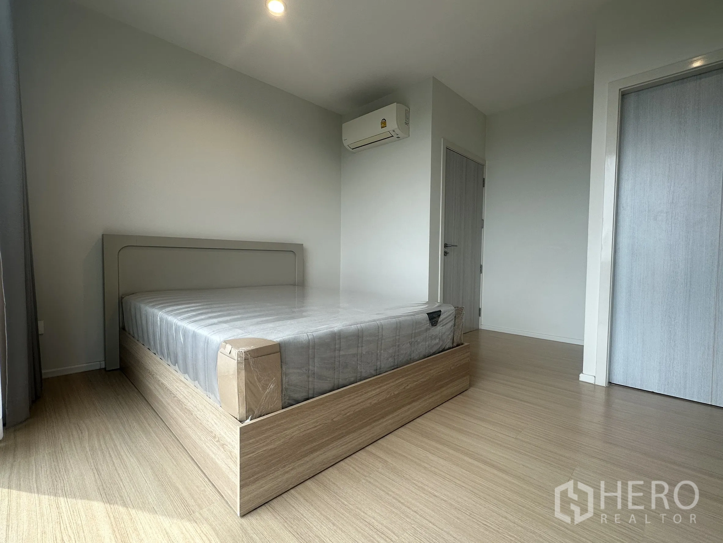 Townhouse for rent in Suan Luang, Bangkok - Bright bedroom with a minimalist bed, wood flooring and air-conditioning.