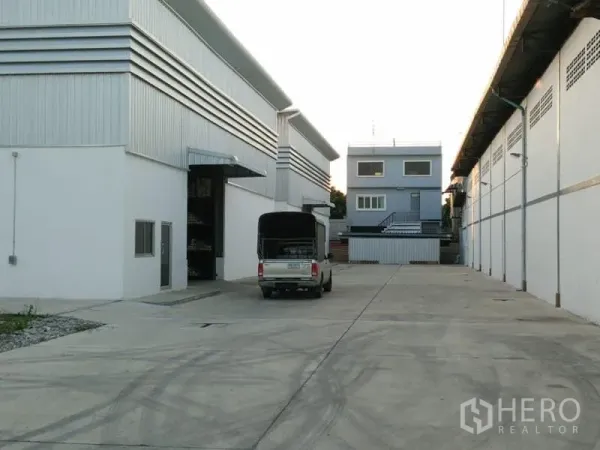 Warehouse for rent in Suan Luang, Bangkok - Wide concrete driveway between warehouse blocks with a pickup truck and an admin building ahead.