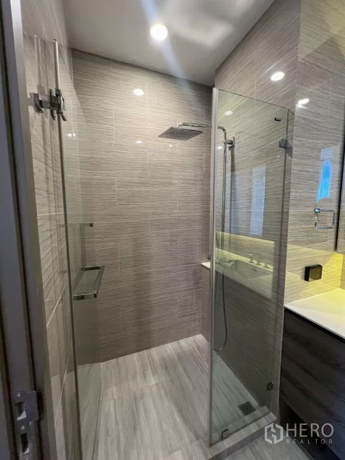 Condominium for rent in Phra Khanong, Bangkok - Glass-enclosed shower room with rain shower and handheld set in tiled bathroom.