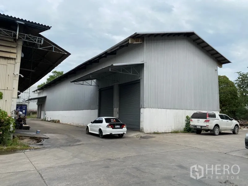 货栈 出租在Khlong Luang, Pathum Thani - 独立仓库斜侧视图，双卷帘门、停车区与园区道路一体。