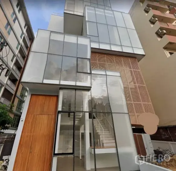 带办公室的家 出租在Phaya Thai, Bangkok - 阿里片区现代多层玻璃立面与木质点缀的家用办公楼外观，可见室内楼梯，位于曼谷帕亚泰。