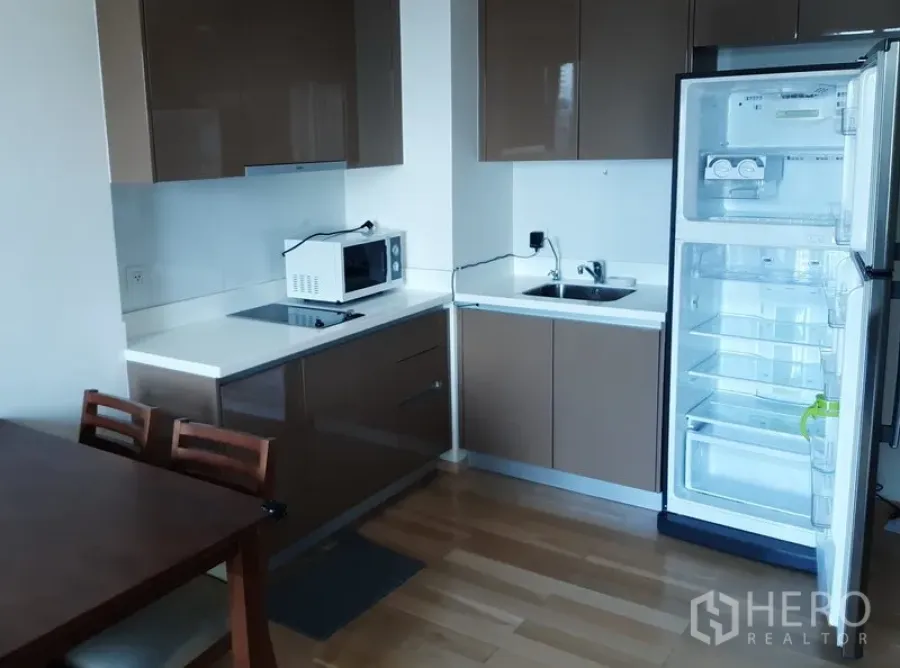 คอนโด ให้เช่าในKhlong Toei, Bangkok - ครัวบิวท์อินสไตล์โมเดิร์นพร้อมตู้ลอย เตาไฟฟ้า ไมโครเวฟ อ่างล้างจาน และตู้เย็นบนพื้นไม้