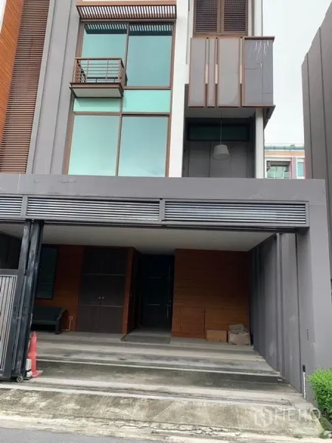 Townhouse for sale in Watthana, Bangkok - Modern multi-storey townhouse facade with floor-to-ceiling windows and a covered carport.
