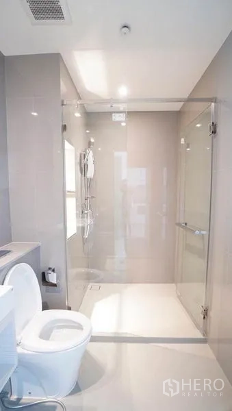 公寓 出售在Khlong Toei, Bangkok - 明亮现代的浴室，玻璃步入式淋浴间、雨淋花洒与白色洁具。