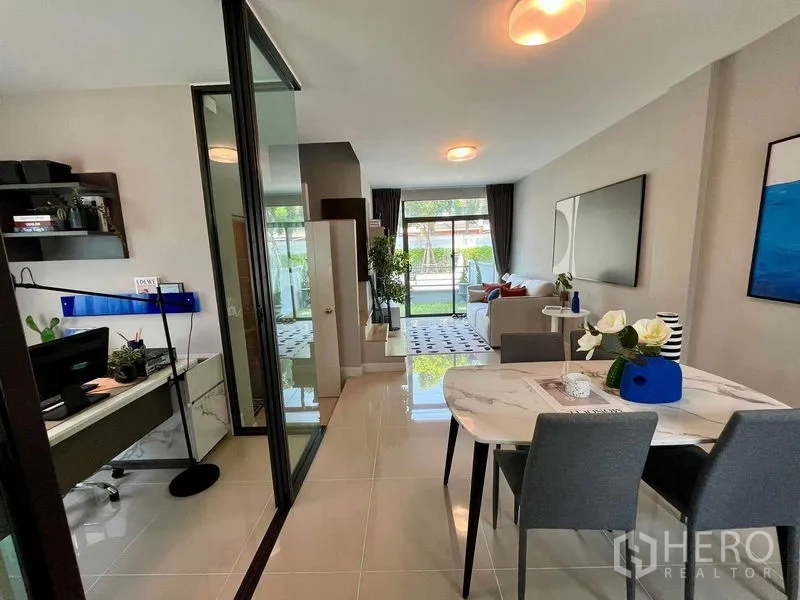Townhouse for sale in Sai Mai, Bangkok - Open-plan living and dining area with a glass-partitioned home office and garden view.