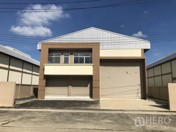 工厂 出租或出售在Pathum Thani - 迷你工厂正面，带卷帘门、二层办公室窗户与金属人字屋顶。