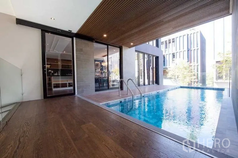 独立式住宅 出售在Prawet, Bangkok - 半室内私人泳池，木质天花与玻璃门连接室内空间。