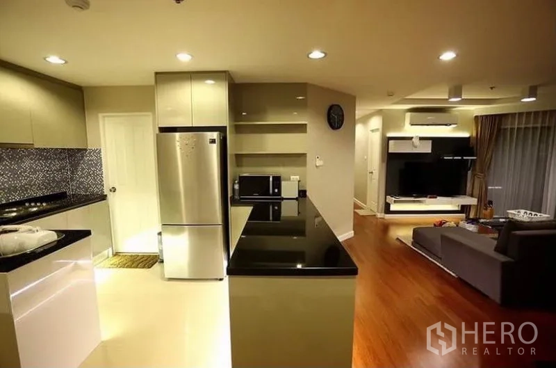 Condominium for rent in Huai Khwang, Bangkok - Open-plan kitchen with black countertops, stainless fridge and a view toward the living area in the Huai Khwang condo.