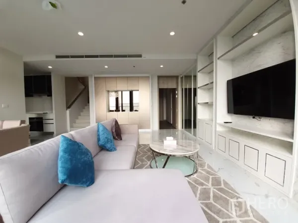 Condominium for rent in Pathum Wan, Bangkok - Contemporary living room featuring a large sectional sofa, built-in shelving and a TV feature wall.