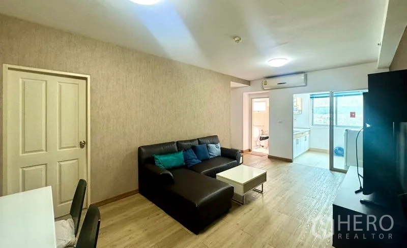 คอนโด ให้เช่าในHuai Khwang, Bangkok - ห้องนั่งเล่นสว่าง พื้นไม้ โซฟาเข้ามุมสีดำ และมองเห็นครัวกับระเบียง