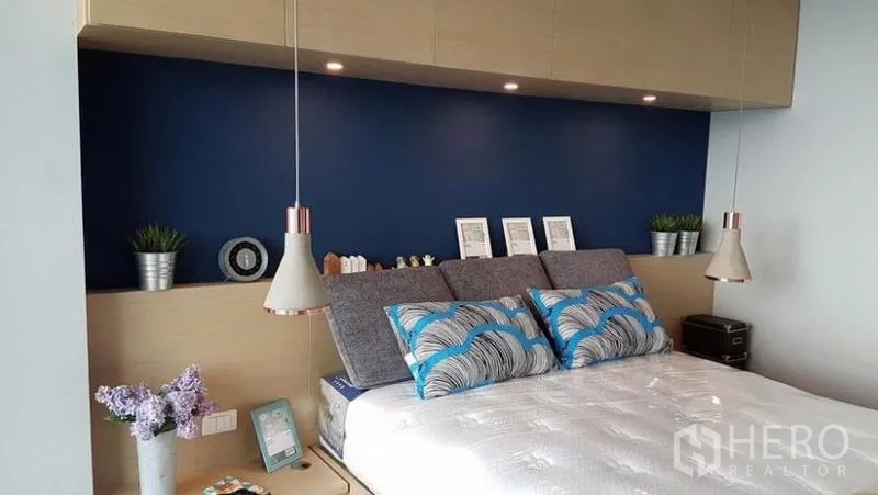 คอนโด ให้เช่าในKhlong San, Bangkok - ห้องนอนหลักผนังสีน้ำเงิน โคมแขวนข้างเตียง และตู้เก็บของบิลท์อินด้านบน