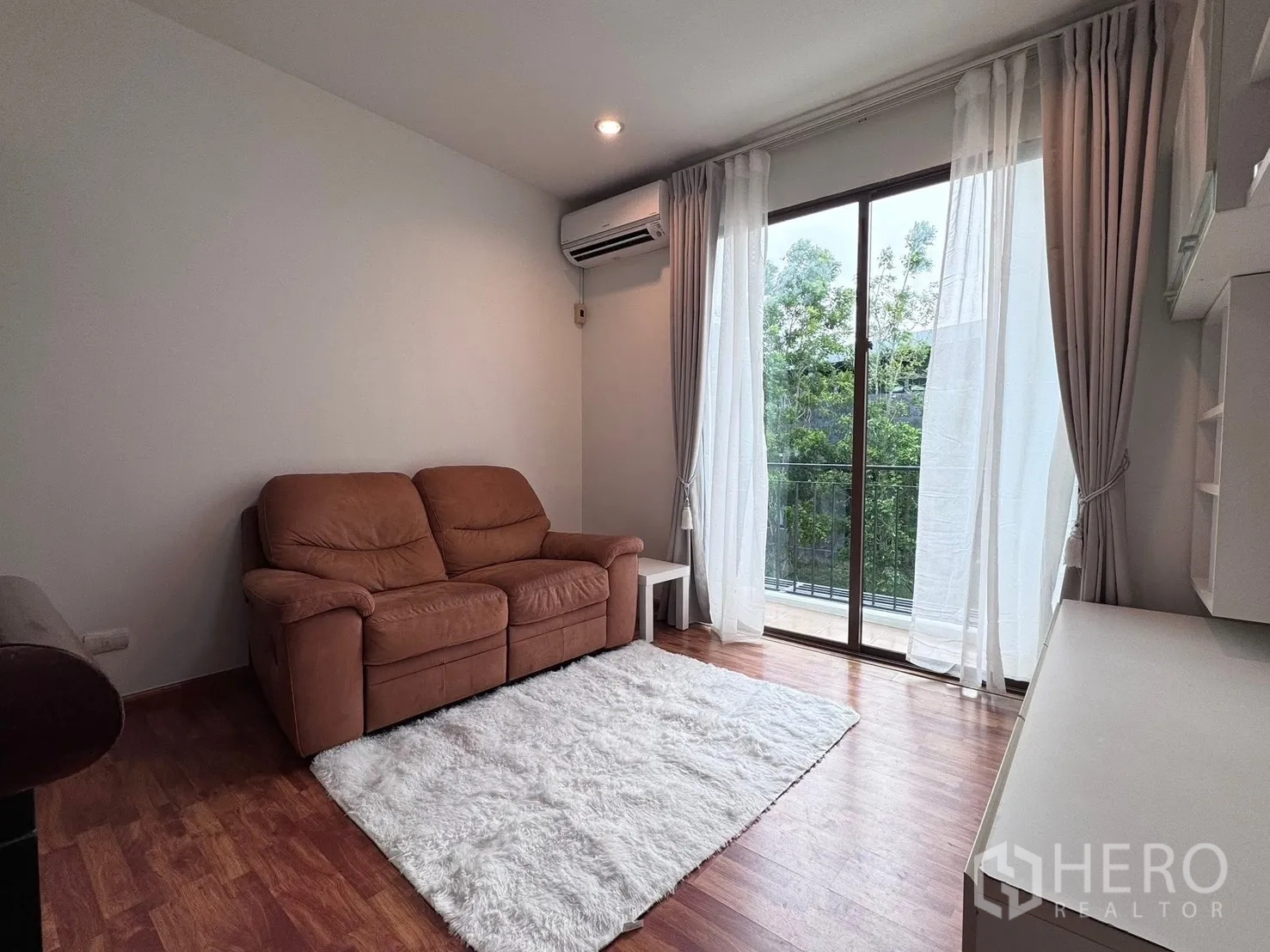 联排别墅 for rent in Phra Khanong, Bangkok - 客厅视角展示沙发、白色地毯和通往阳台的移门。