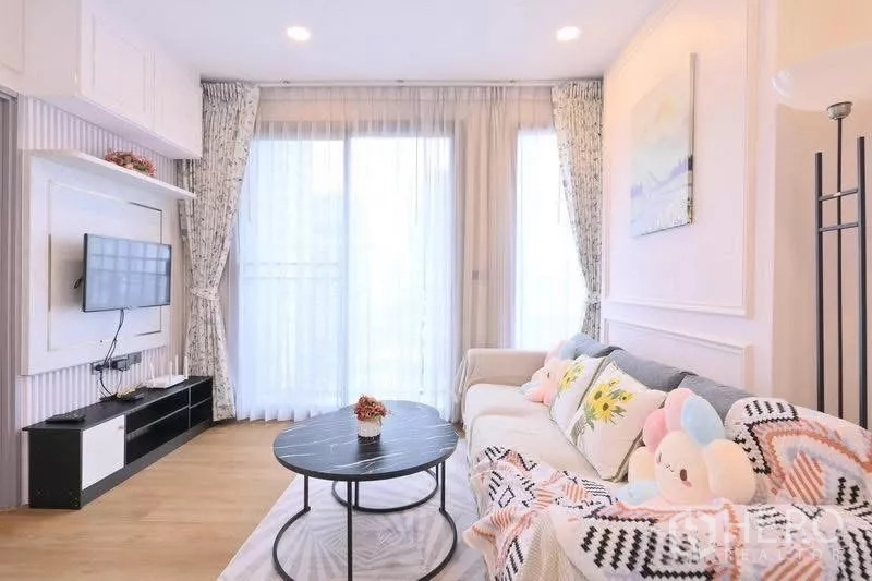 Condominium for rent in Watthana, Bangkok - Cozy sitting area with large windows, wall‑mounted TV and modern sofa bathed in natural light.