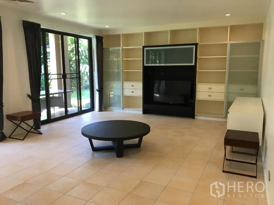 Detached House for rent in Watthana, Bangkok - Living room with built-in shelving and TV unit, large sliding doors leading to the green garden.