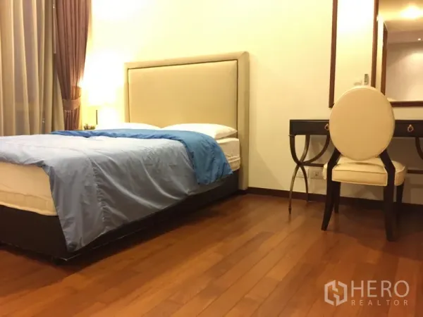 Condominium for rent in Khlong Toei, Bangkok - Cozy bedroom with upholstered headboard, vanity desk, wooden floors and large window curtains.