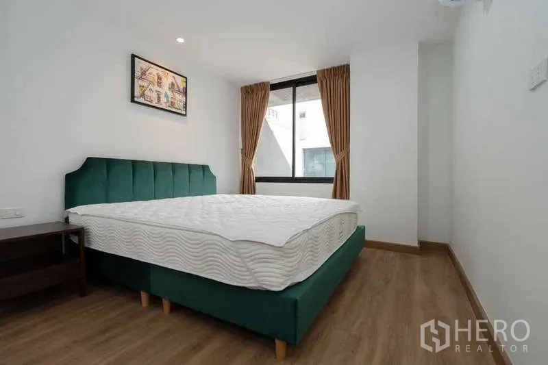 Apartment for rent in Khlong Toei, Bangkok - Second bedroom with green upholstered bed, window and wood floors.
