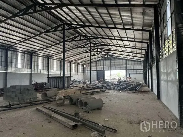 工厂 出租在Phan Thong, Chon Buri - 工厂内部宽敞，高跨钢梁与侧窗采光，地面放置建材。