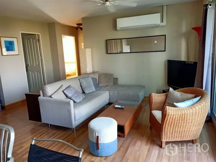 คอนโด ให้เช่าในKhlong Toei, Bangkok - มุมนั่งเล่นอบอุ่นด้วยโซฟาเข้ามุม เก้าอี้หวาย ทีวี และกระจกยาวบนผนัง