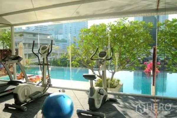 คอนโด ให้เช่าหรือขายในWatthana, Bangkok - ห้องฟิตเนสผนังกระจก มีจักรยานออกกำลังกายและลู่วิ่ง มองเห็นสระว่ายน้ำและต้นไม้